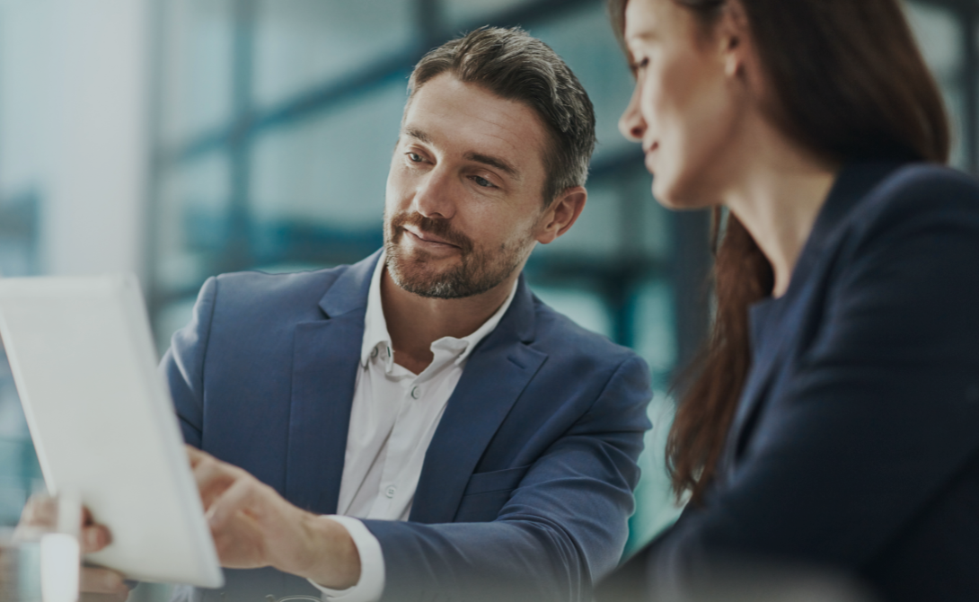 Two professionals discussing payroll topics while viewing a tablet – representing key considerations when outsourcing payroll and salary administration.