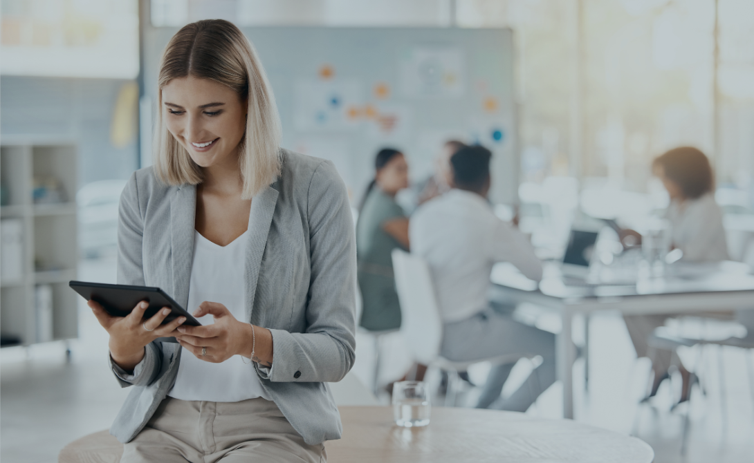 Smiling woman using a tablet in a modern office – representing digital HR services and software from hire to retire.