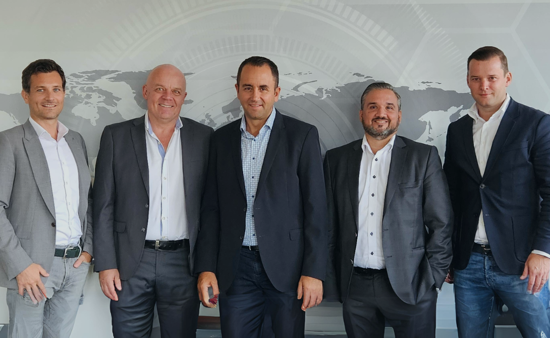 Five business professionals standing in front of a world map graphic – representing the integration of Sowatec AG into the CONVOTIS Group.