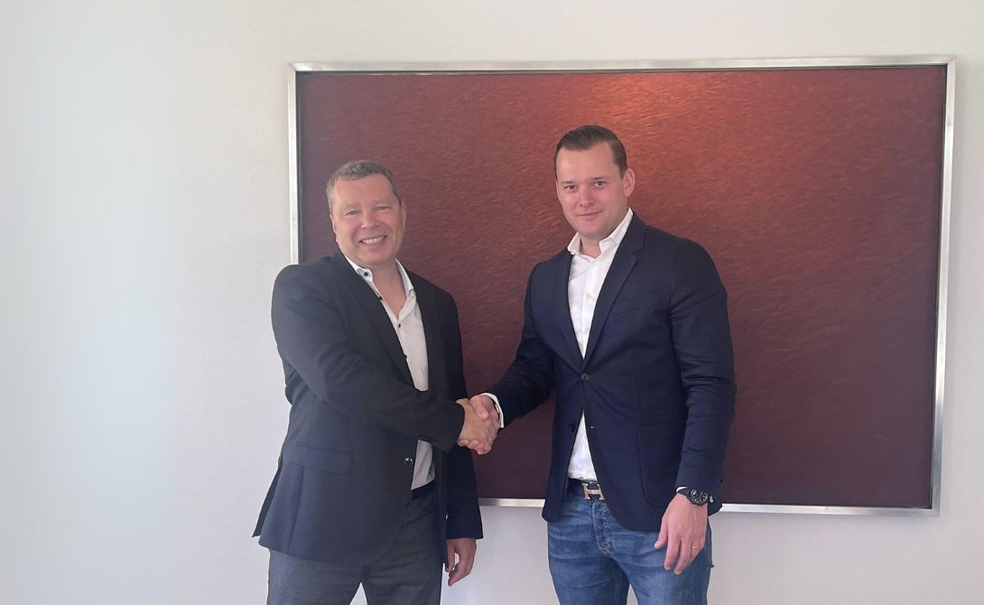 Two business professionals shaking hands in front of a red background – symbolizing the integration of Agentil into the CONVOTIS Group.
