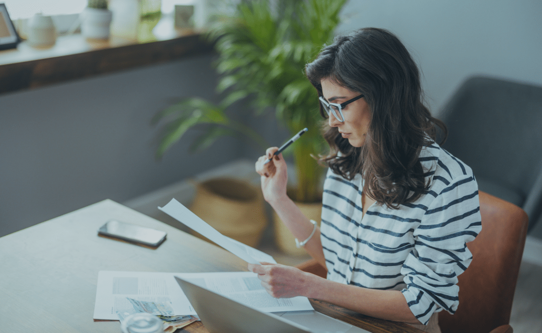 Woman reviewing documents at a home desk with a laptop – representing challenges and solutions in IT consulting for the tax advisory sector.