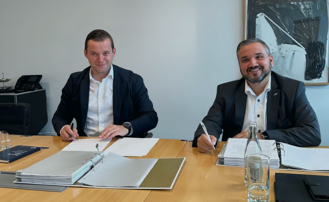 Two business professionals signing documents at a table – symbolizing the expansion of the CONVOTIS Group through the integration of JMC.