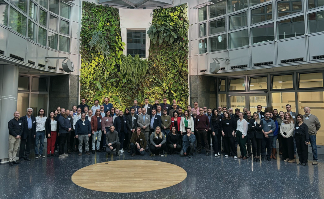 Large group photo of project participants in a modern atrium with green wall – representing CONVOTIS’s contribution to European AI innovation through the DeployAI initiative.