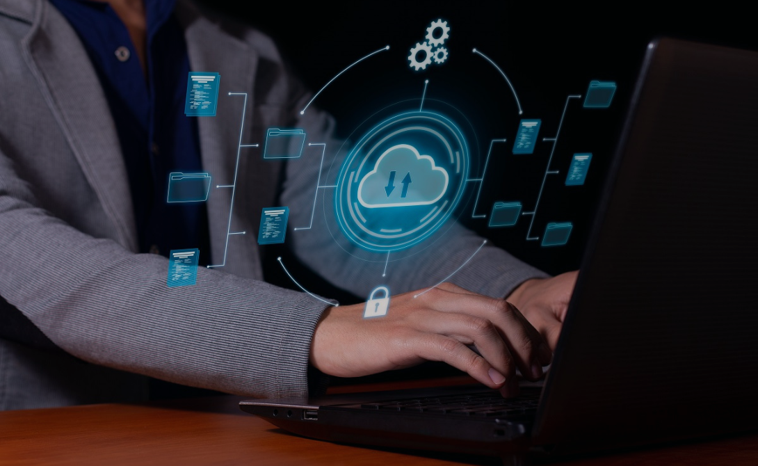 Person typing on a laptop with a digital cloud interface hovering above, symbolizing the comparison between self-managed and managed private cloud models.