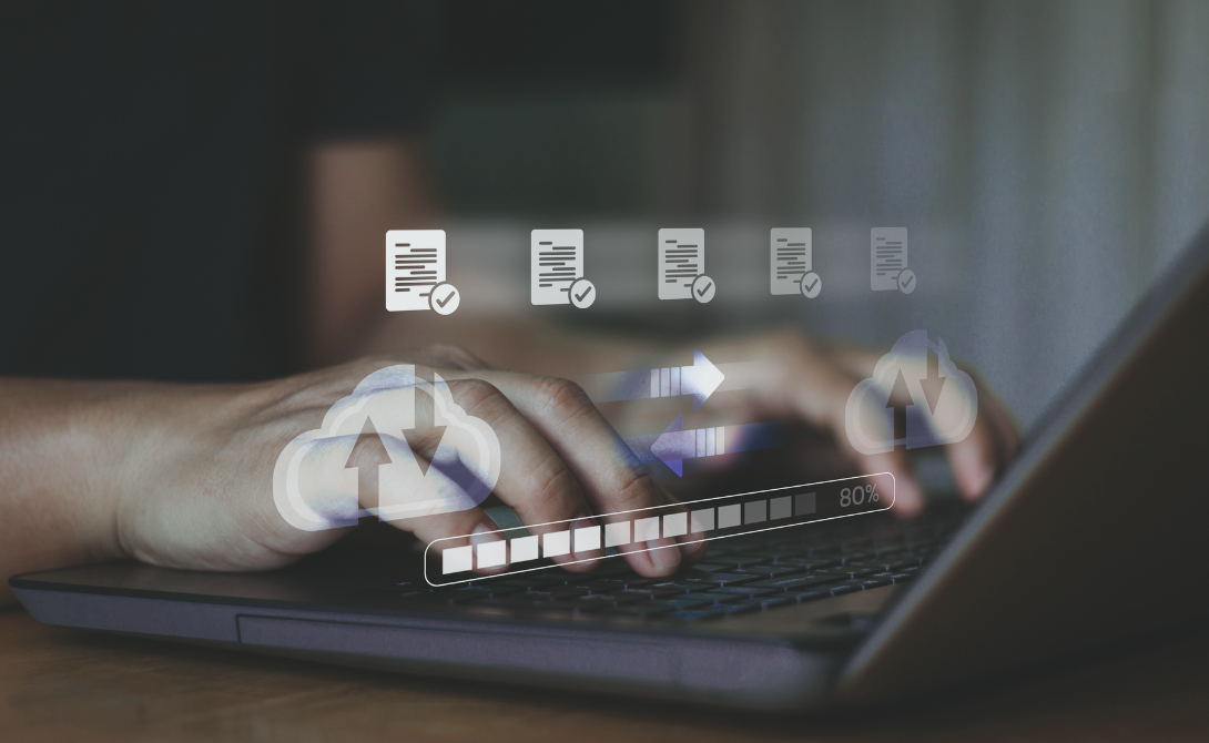 Hands typing on a laptop with cloud and file transfer icons representing automated cloud backup and data synchronization.